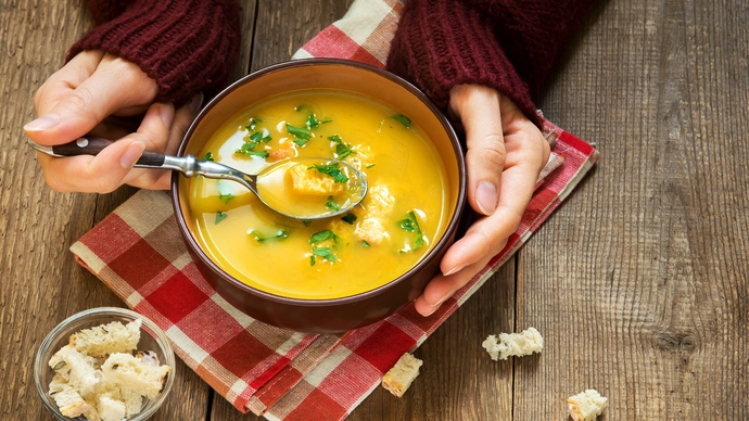 Hands in gloves, one holding a spoon and the other holding a bowl of lentil soup