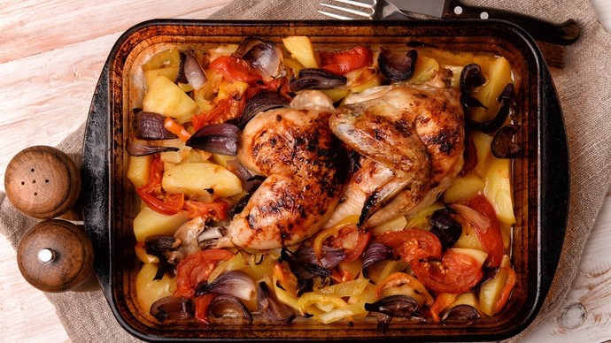 a traybake containing a crispy whole roast chicken surrounded by a variety of roasted bright vegetables