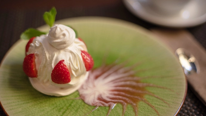 A merigue topped with halved stawberries on a green plate with fruit sauce