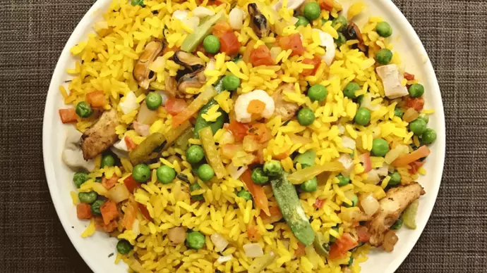 A vibrant bowl of yellow rice paella with garden peas and other assorted vegetable pieces