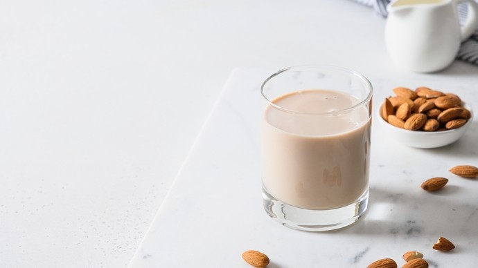 A glass of almond milk next to a handful of whole almonds 