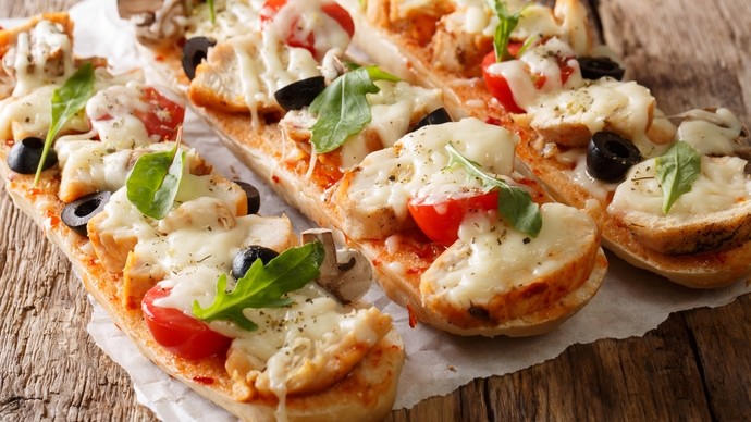 Pizzas made on bread cut lenghways with vegetable and cheese topping