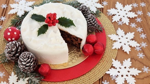 An iced and decorated Christmas cake with a slice missing and surrounded by decorations