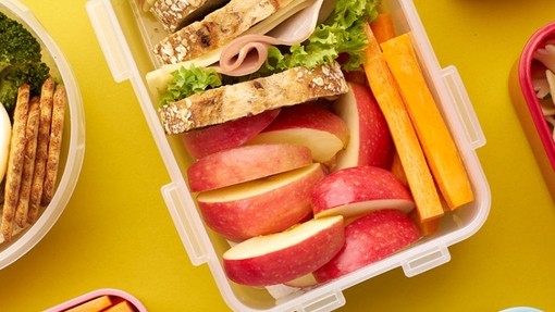 Three lunchboxes with different lunches inside - sandwiches, pasta, fruit and veg