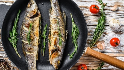 Two sea bass cooking in a frying pan with herbs