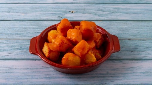 A small bowl of cubed patatas bravas covered in brown sauce