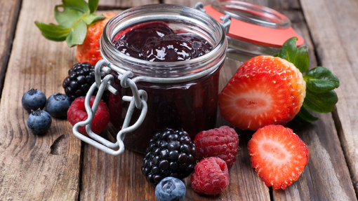 a jar of thick purple berry jam surrounded by an assortment of fresh berries