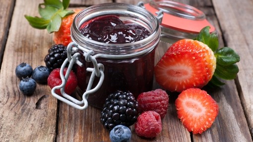 a jar of thick purple berry jam surrounded by an assortment of fresh berries