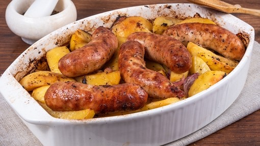 A dish of baked sausages and potatoes on a table ready to serve