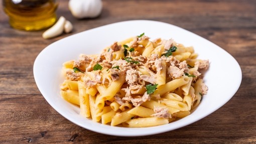 a bowl of golden pasta mixed with tuna flakes and topped with a herb garnish
