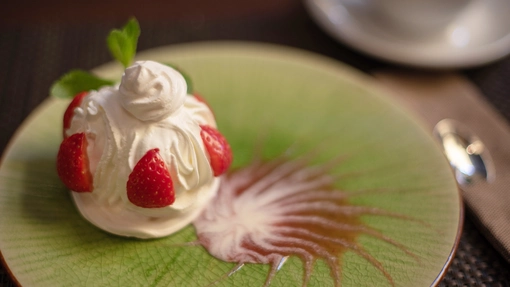 A merigue topped with halved stawberries on a green plate with fruit sauce