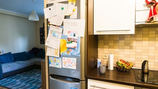 A fridge covered in magnets, paperwork and pictures in a family kitchen