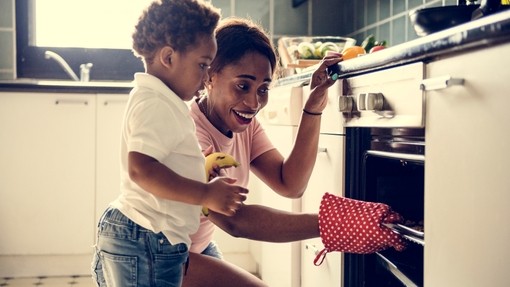 A mother and child cooking together, the mum is putting a tray in the oven