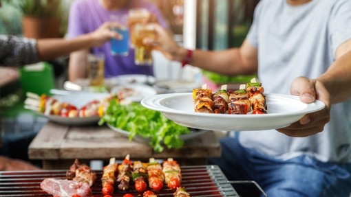 A person holding out a plate of kebabs at a BBQ