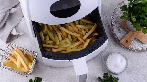An air-fryer showing an open drawer full of chips, with leafy herbs dotted around the image.