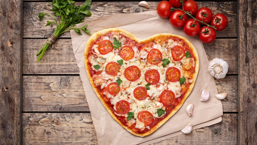 A heart shaped pizza with tomatoes, garlic and green herbs dotted around