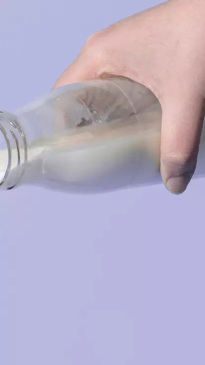 Someone pouring milk down the sink from a glass bottle
