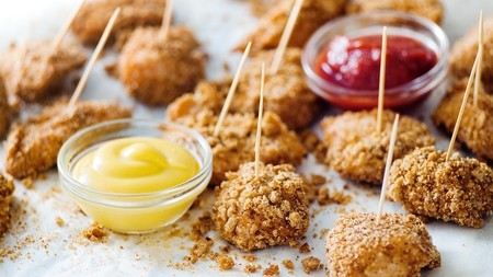 Multiple golden crispy pieces of chicken on skewers with dipping sauces