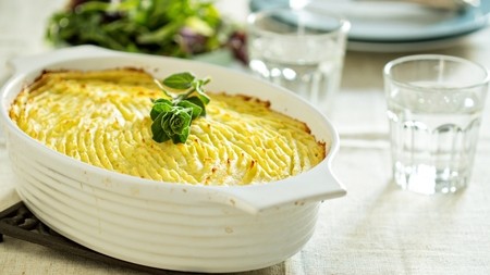 A golden shepherd's pie in a white ceramic dish topped with a green garnish