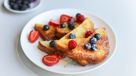 A white plate with slices of French toast, topped with honey and fruit