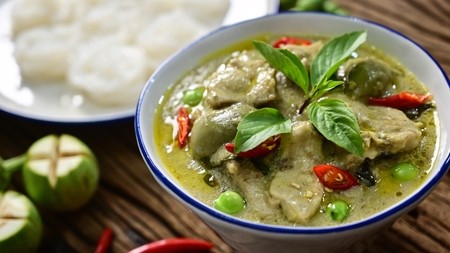 a rich green thai curry mixed with chicken pieces and tomatoes and peas