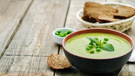 a creamy pastel green bowl of pea and mint soup topped with fresh mint