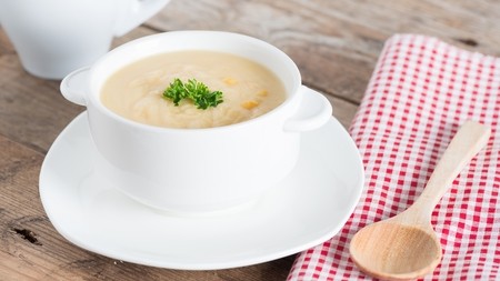 A white bowl of thick potato soup topped with parsley