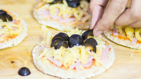 Preparation of a mini pizza topped with cheese, tomato sauce, ham and olives