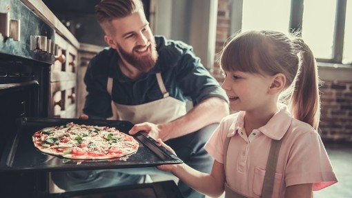 Dad and kid taking a cooked pizza out of oven