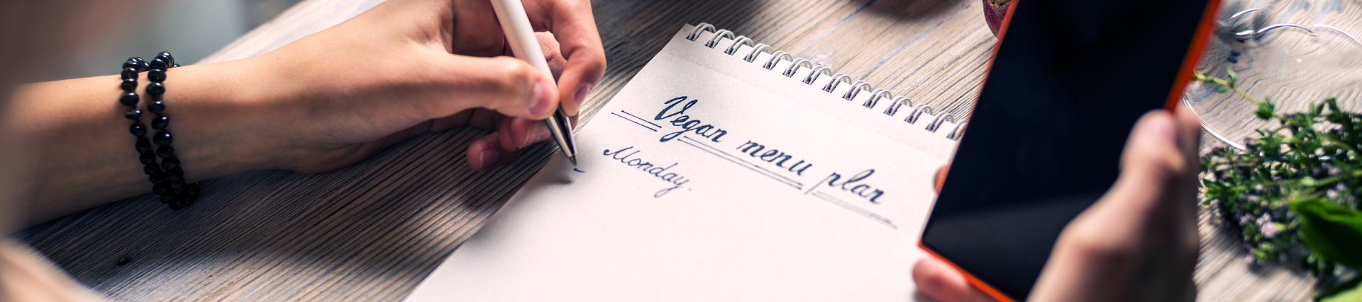 A person using a phone and notepad to write a meal plan