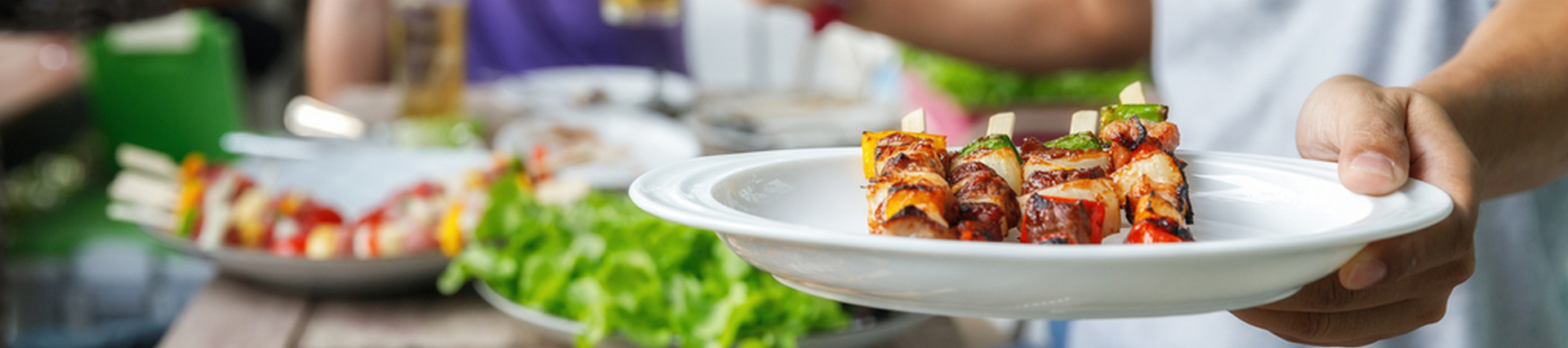 A person holding out a plate of kebabs at a BBQ