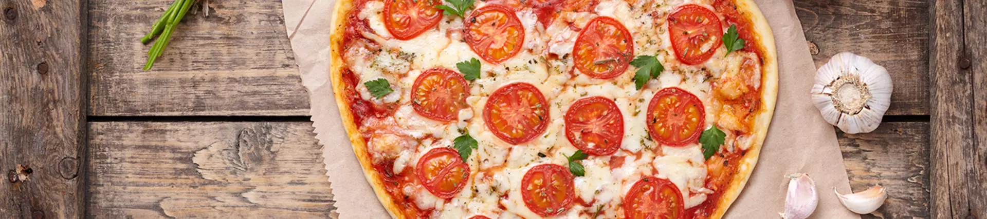 A heart shaped pizza with tomatoes, garlic and green herbs dotted around